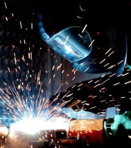 A focused welder works with metal in an industrial setting, creating vibrant sparks.